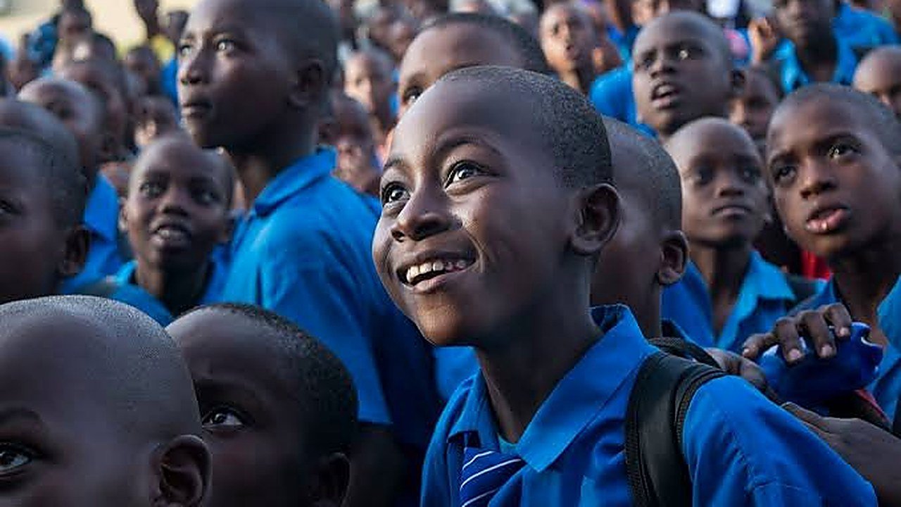 A crowd of African schoolchildren in blue uniforms, one of them smiling as he looks up